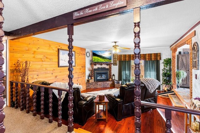 living area featuring a textured ceiling, a glass covered fireplace, beam ceiling, and wooden walls