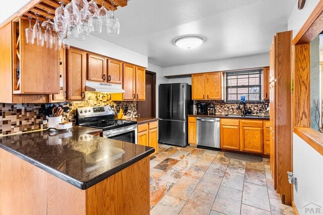 kitchen with pendant lighting, appliances with stainless steel finishes, a sink, a peninsula, and under cabinet range hood