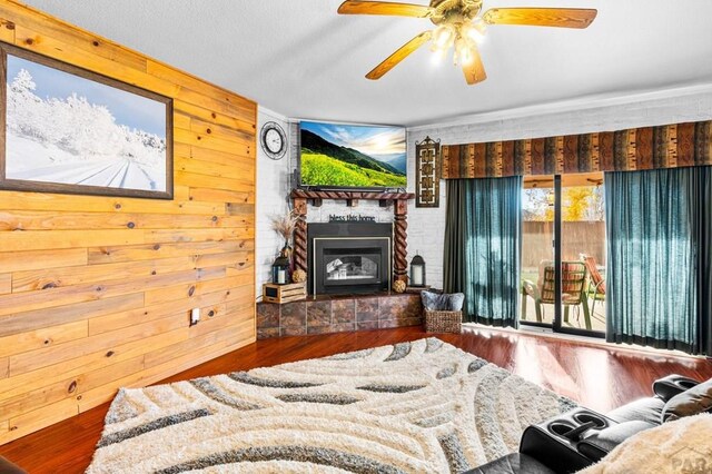 living area featuring wooden walls, a fireplace, a ceiling fan, and wood finished floors