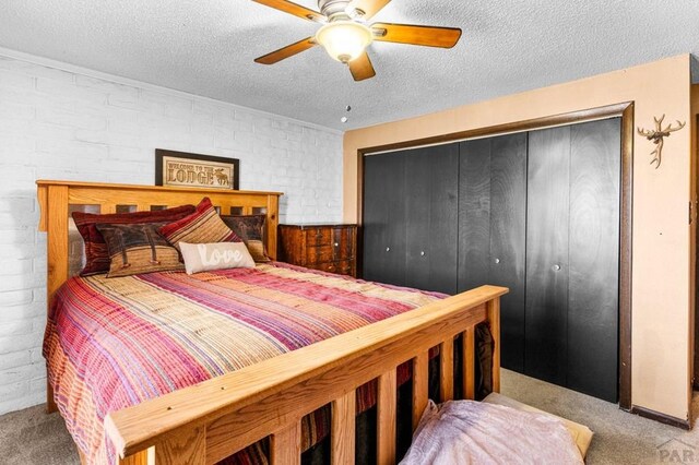 bedroom featuring a textured ceiling, light colored carpet, brick wall, a ceiling fan, and a closet