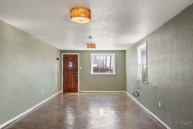 foyer entrance featuring baseboards, a textured ceiling, and a textured wall