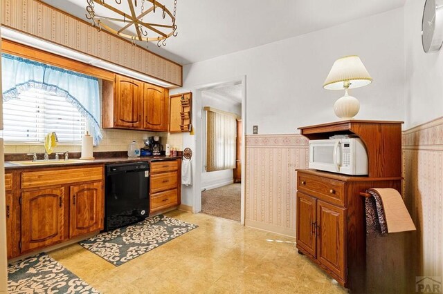 kitchen featuring brown cabinetry, dishwasher, white microwave, a wainscoted wall, and a sink