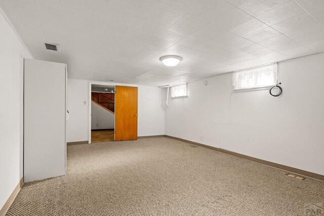 basement with baseboards, visible vents, and light colored carpet