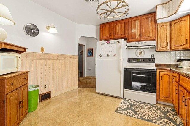 kitchen featuring arched walkways, under cabinet range hood, white appliances, brown cabinets, and wallpapered walls