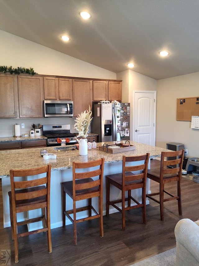 kitchen featuring a breakfast bar, dark wood-style flooring, appliances with stainless steel finishes, vaulted ceiling, and light stone countertops