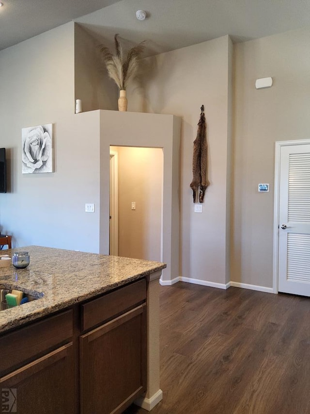 kitchen with light stone counters, dark wood-style flooring, dark brown cabinetry, and baseboards