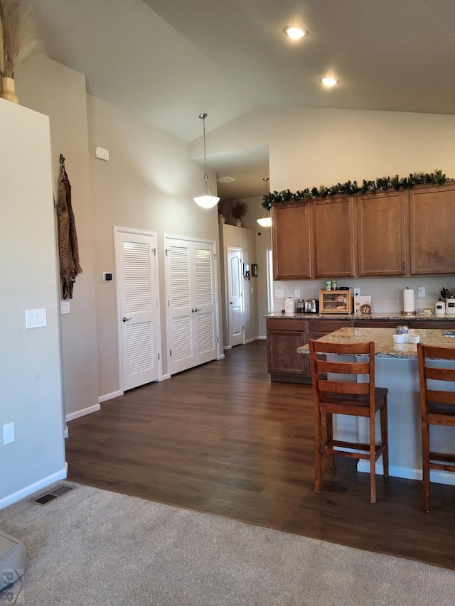 kitchen featuring a breakfast bar, pendant lighting, brown cabinets, dark wood finished floors, and vaulted ceiling