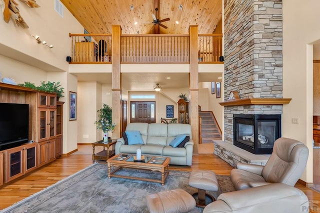 living area featuring light wood-style floors, a stone fireplace, and a ceiling fan