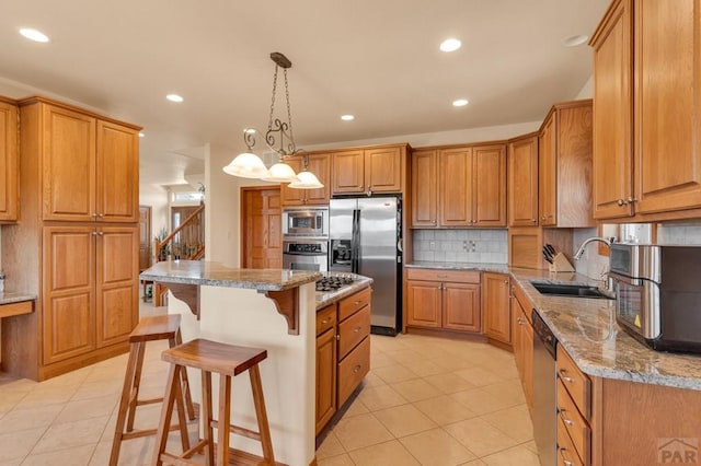 kitchen featuring brown cabinetry, appliances with stainless steel finishes, light stone counters, a center island, and a sink