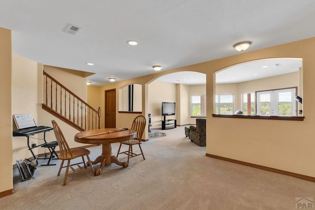 interior space with light carpet, baseboards, visible vents, arched walkways, and stairs