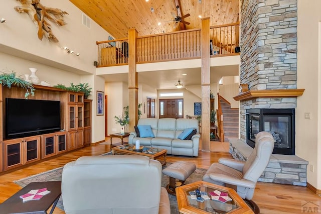 living room featuring wooden ceiling, visible vents, a stone fireplace, and wood finished floors