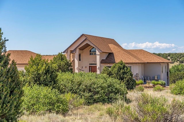 view of front of house with roof with shingles, central AC, and stucco siding