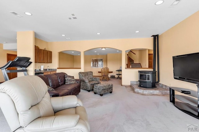 living area featuring visible vents, arched walkways, light colored carpet, a wood stove, and recessed lighting