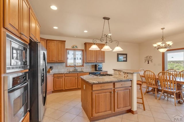 kitchen with light stone counters, a center island, stainless steel appliances, pendant lighting, and a sink