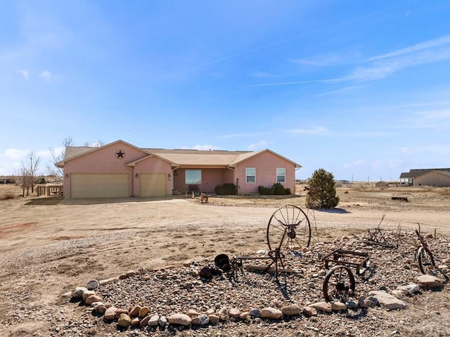 view of front of house with dirt driveway, an attached garage, and stucco siding