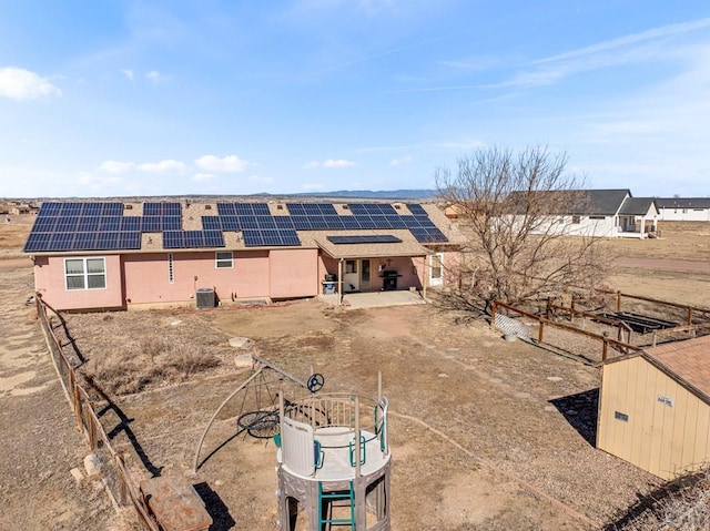 back of house featuring roof mounted solar panels, fence, central AC, and stucco siding