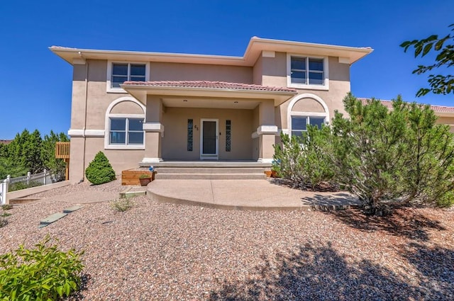 rear view of property featuring a porch, fence, a tiled roof, and stucco siding