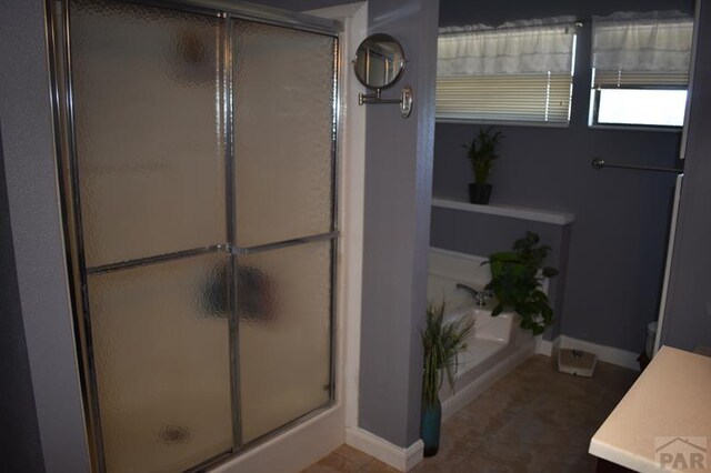 bathroom with a stall shower, vanity, baseboards, and a bath