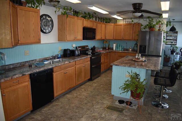 kitchen with a kitchen island, brown cabinetry, a sink, and black appliances