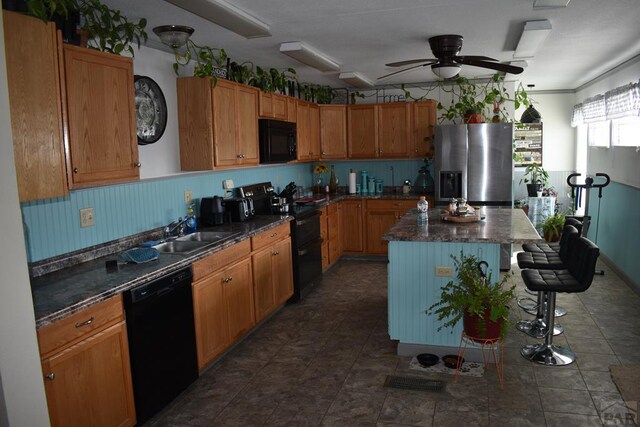 kitchen with brown cabinets, dark countertops, a kitchen island, a sink, and black appliances