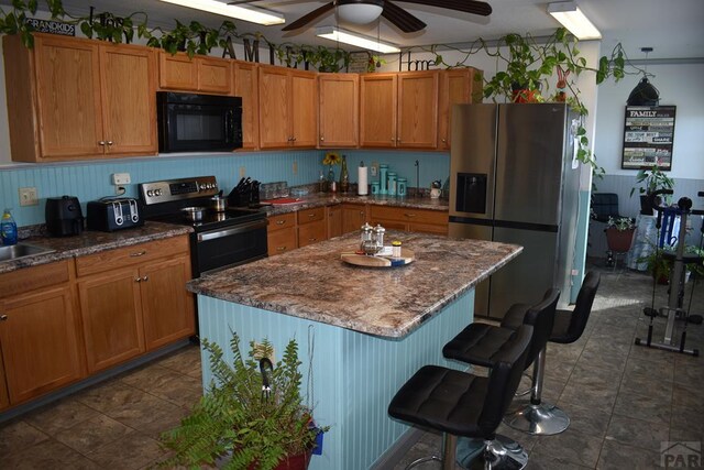 kitchen featuring appliances with stainless steel finishes, brown cabinetry, a kitchen island, and a ceiling fan