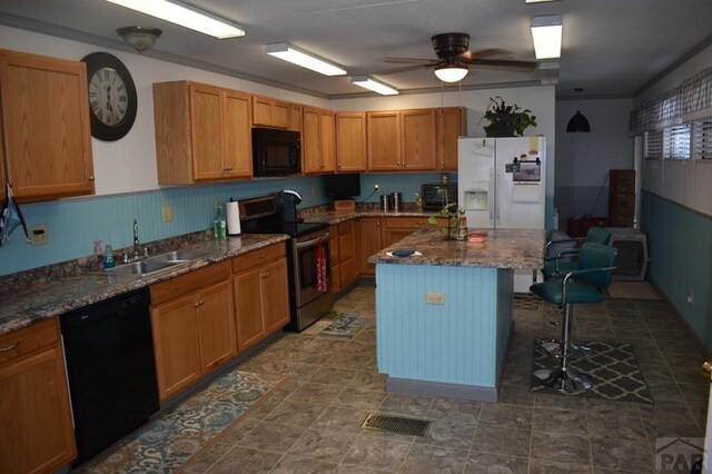 kitchen with brown cabinetry, a kitchen breakfast bar, a center island, black appliances, and a sink