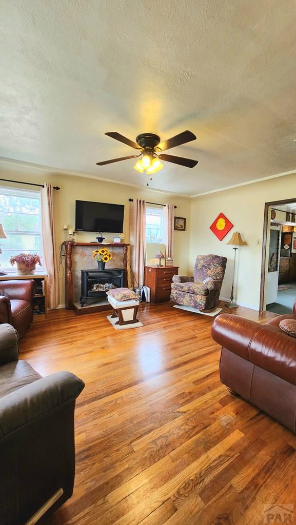 2631 Cedar St, Pueblo, CO 81004 - living room featuring a textured ceiling, wood finished floors, a fireplace with raised hearth, and ceiling fan