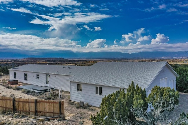 back of house with central air condition unit, a deck with mountain view, fence, and roof with shingles