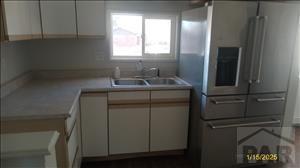 kitchen with stainless steel fridge, white cabinets, light countertops, and a sink