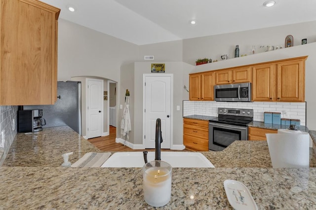1284 N Challenger Dr, Pueblo West, CO 81007 - kitchen with stainless steel appliances, decorative backsplash, light stone counters, a sink, and lofted ceiling