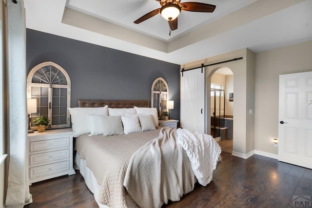 4288 Cedarweed Blvd, Pueblo, CO 81001 - bedroom featuring a barn door, arched walkways, a tray ceiling, and dark wood finished floors