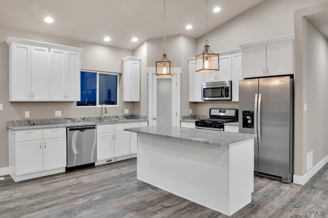 kitchen featuring decorative light fixtures, light wood-style flooring, appliances with stainless steel finishes, white cabinetry, and a kitchen island