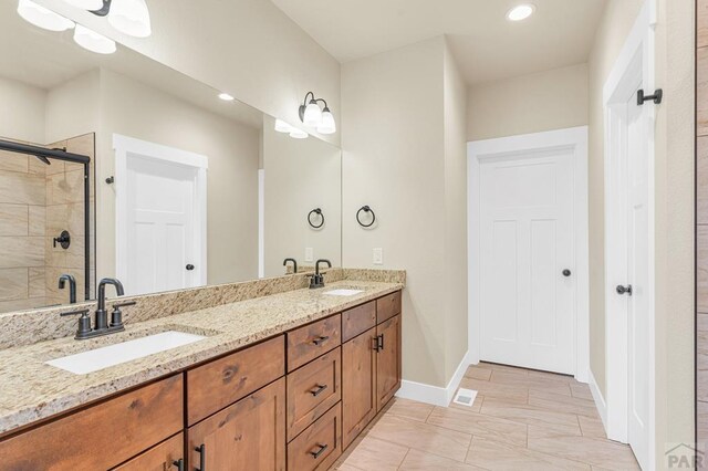 bathroom with double vanity, a shower stall, baseboards, and a sink