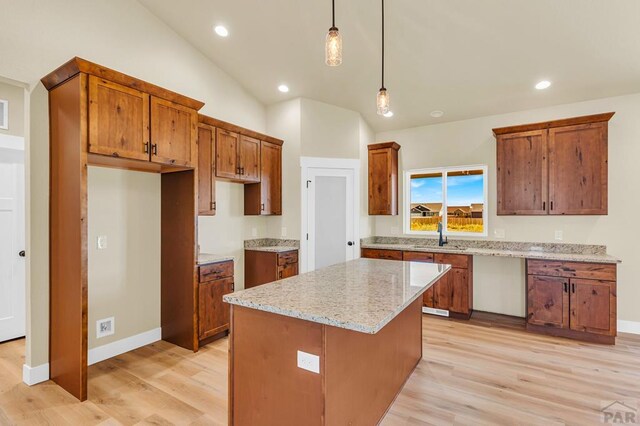 kitchen with light stone counters, vaulted ceiling, a center island, brown cabinetry, and pendant lighting