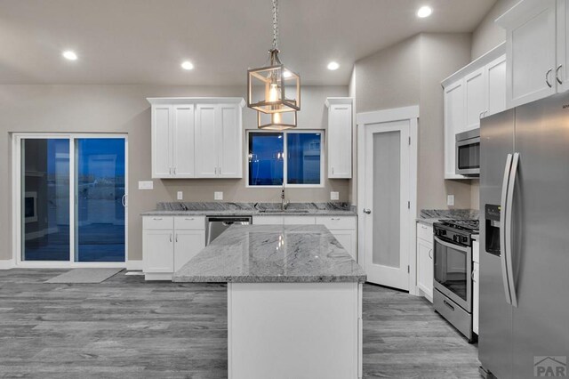 kitchen with a kitchen island, appliances with stainless steel finishes, light stone countertops, white cabinetry, and pendant lighting