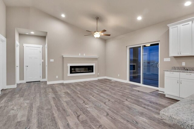 unfurnished living room featuring recessed lighting, light wood-style flooring, vaulted ceiling, and a glass covered fireplace