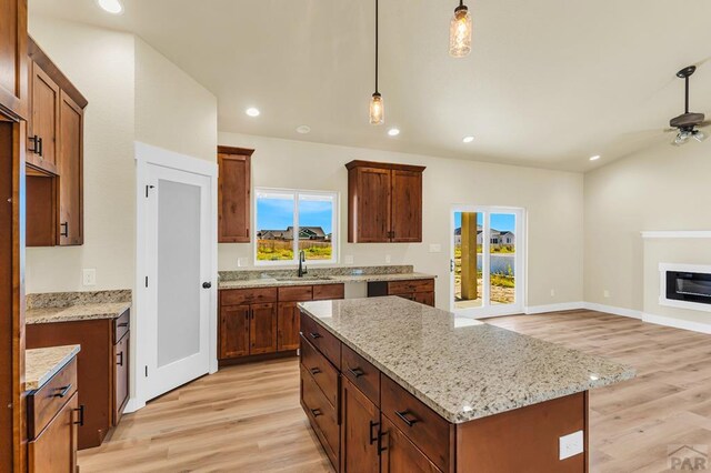 kitchen featuring hanging light fixtures, a glass covered fireplace, a kitchen island, a sink, and light wood-type flooring