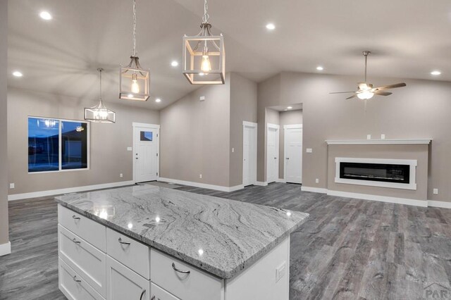 kitchen with light stone counters, pendant lighting, a glass covered fireplace, open floor plan, and white cabinets