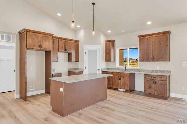 kitchen with visible vents, brown cabinetry, a center island, light stone countertops, and pendant lighting