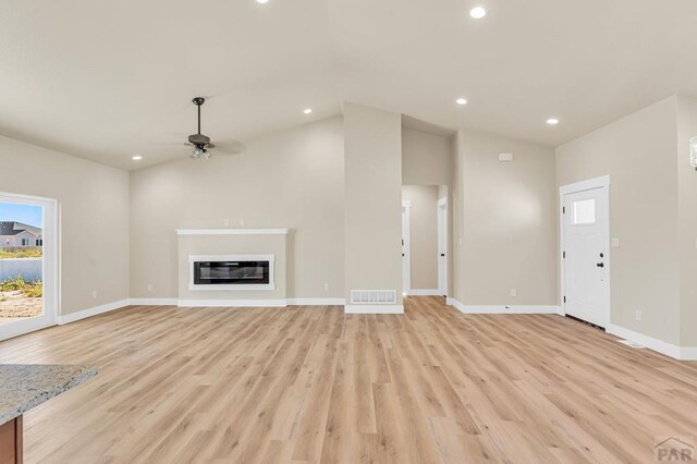 unfurnished living room featuring lofted ceiling, light wood-style flooring, recessed lighting, visible vents, and a glass covered fireplace