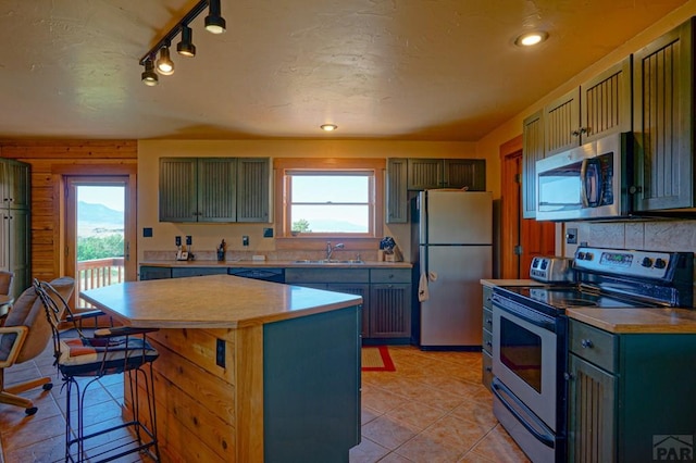 kitchen featuring a sink, light countertops, appliances with stainless steel finishes, a center island, and a kitchen bar