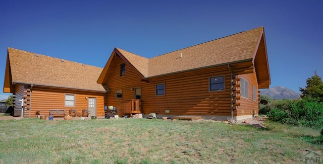 back of house featuring roof with shingles, a lawn, log siding, and a mountain view