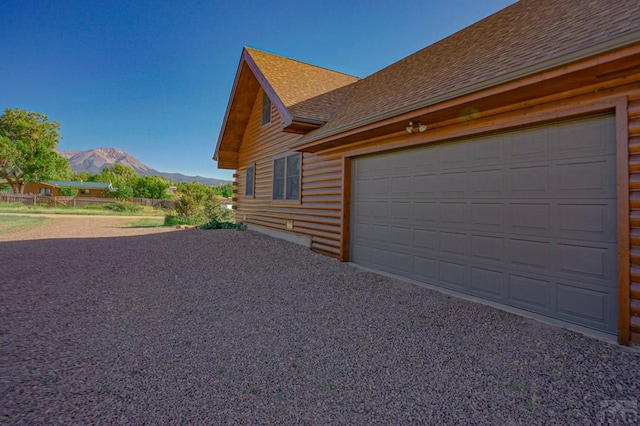 view of side of home with gravel driveway, a shingled roof, a mountain view, log exterior, and a garage