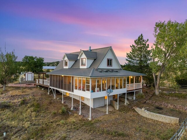 back of house at dusk with a storage shed, a sunroom, metal roof, a garage, and driveway