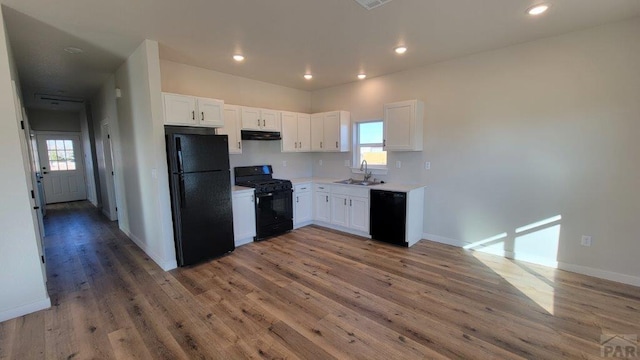 kitchen with under cabinet range hood, light wood-style floors, white cabinets, black appliances, and a sink