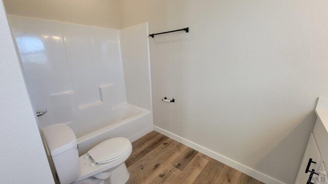 full bath featuring toilet, shower / tub combination, wood finished floors, baseboards, and vanity