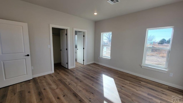 unfurnished bedroom featuring visible vents, baseboards, wood finished floors, and a spacious closet