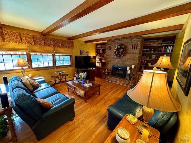 living area featuring beam ceiling, a brick fireplace, and wood finished floors