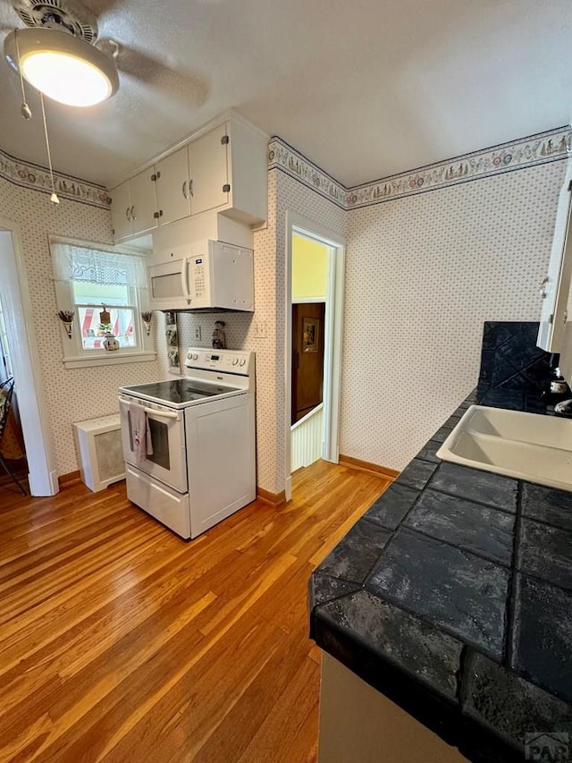 kitchen with light wood-style floors, white appliances, white cabinetry, a sink, and wallpapered walls