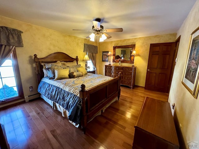 bedroom with ceiling fan, a baseboard heating unit, wood-type flooring, and baseboards